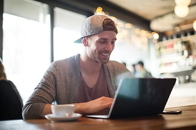 Smiling man looking at laptop in coffee shop