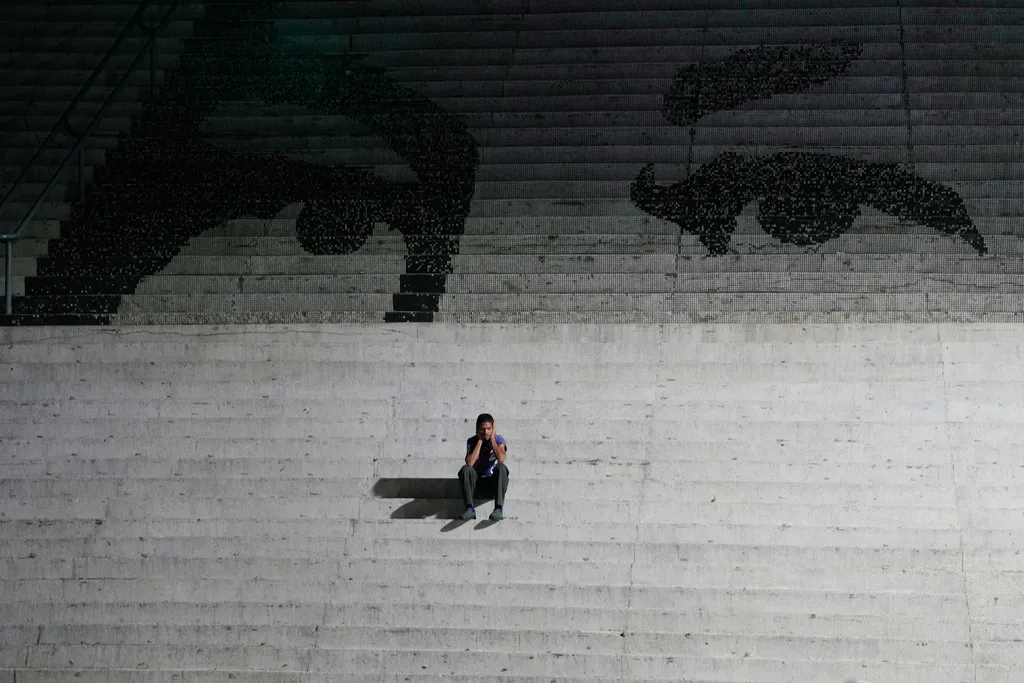 A person sits alone on wide concrete steps beneath a large artistic depiction of two eyes on the upper stairs.