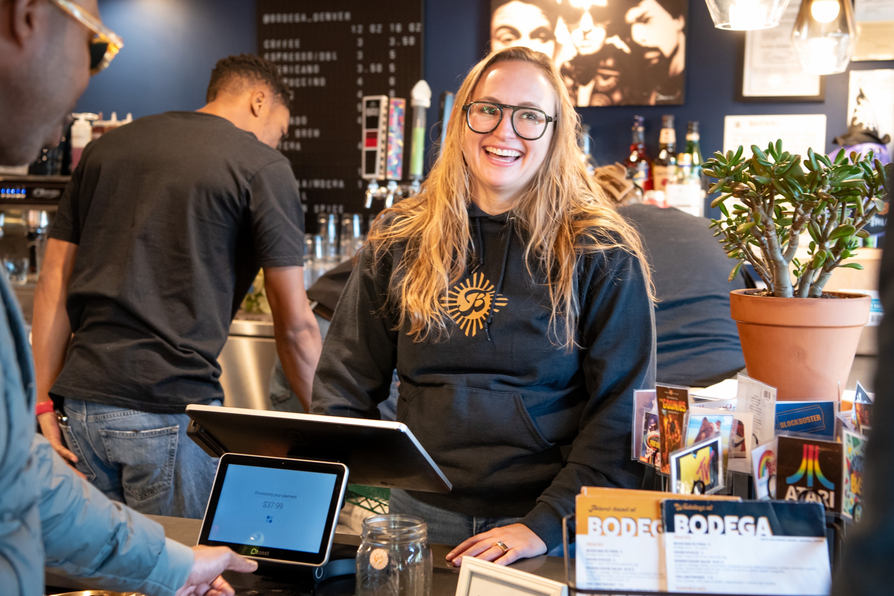 blonde woman with glasses smiles at a restaurant check out counter