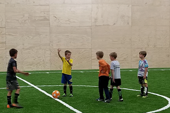photo of three kids playing soccer on turf