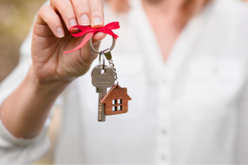 Person holding a keychain with a key, house-shaped charm, and ribbon