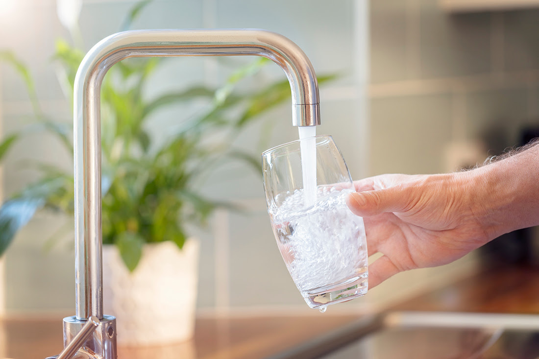 Hand holding glass into which water is pouring into a sink faucet