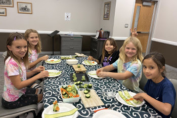 kids sitting at a table learning how to roll sushi