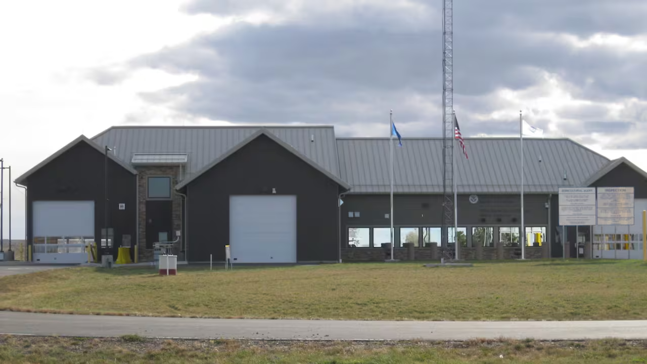 A large building with two garage doors and windows into office space sits on green grass with flags in front.