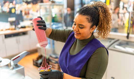 Smiling food service employee preparing ice cream at a counter.