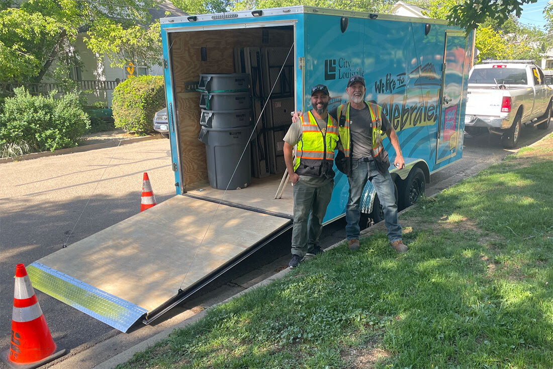Two City of Louisville employees smiling in front of Block Party Trailer