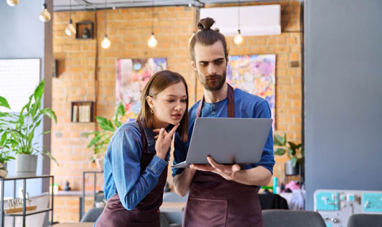 Young man and woman workers owners in aprons using laptop, inside restaurant café.