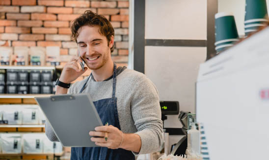 Small business owner smiles while looking at a report and talking on the phone.