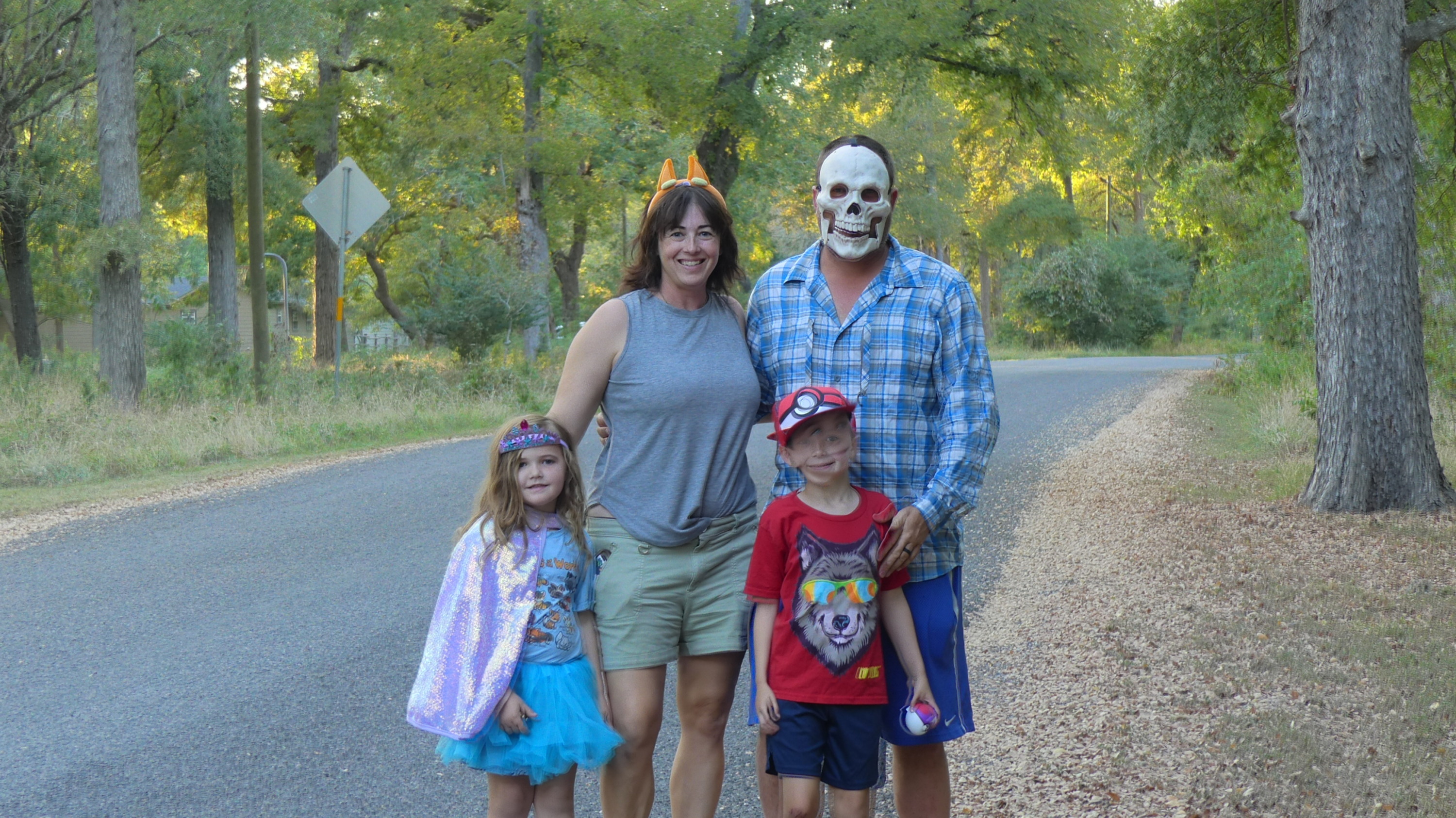 family of four in halloween costumes in front of a road and surrounded by woods