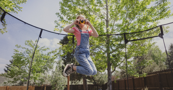 Girl jumping on trampoline while taking photo with disposable camera