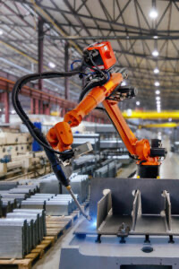 Orange industrial robot arm welding a metal part