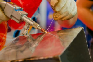 Welder hands in gloves using portable handheld laser welding machine with bright sparks flying