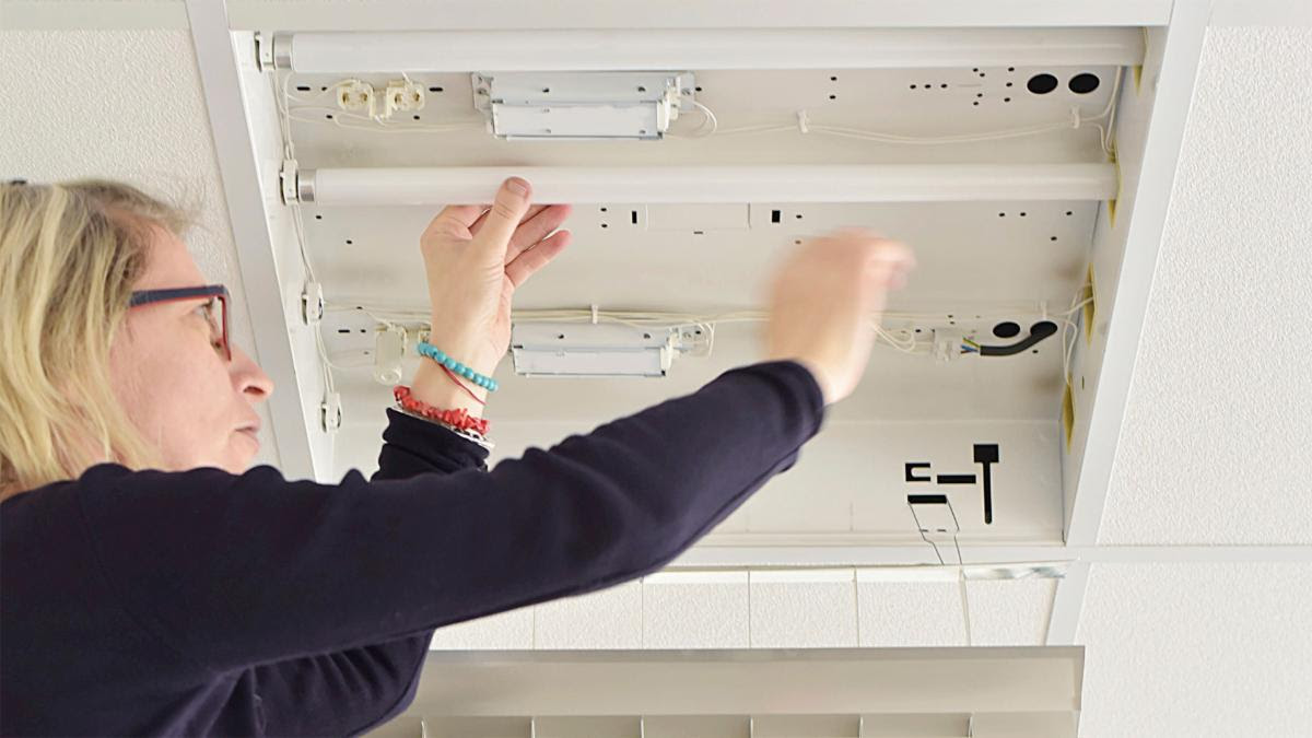 A woman is putting an LED light into a commercial light fixture.