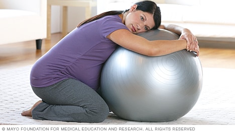Mujer en trabajo de parto arrodillada sobre la pelota para el parto