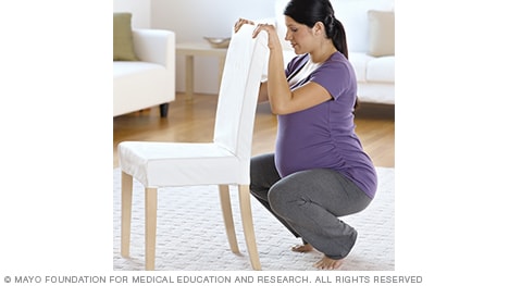 Mujer en trabajo de parto haciendo sentadillas sujetándose a una silla
