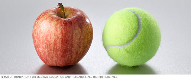 A small apple next to a tennis ball.