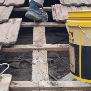 אדם עומד על גג רעפים עם דלי צהוב