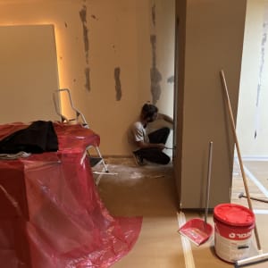 אדם עובד על קיר, דלי צבע, יריעת פלסטיק אדומה