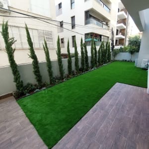 גינה מעוצבת עם דשא סינטטי ושורת עצי ברוש כגדר חיה