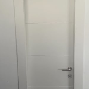 דלת פנים לבנה מעוצבת עם פסי חריטה וידית מתכתית