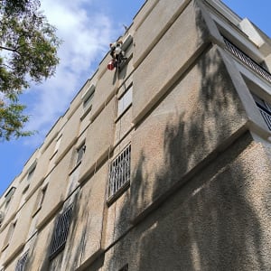 אדם עובד בגובה על בניין עם חבלים וציוד בטיחות