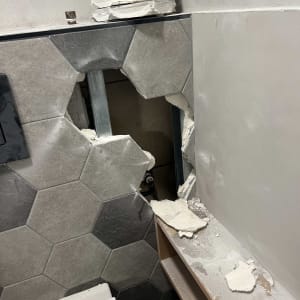 קיר שבור עם אריחים שבורים וצינור חשוף