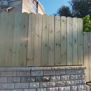 גדר עץ גבוהה על קיר אבן בגינה