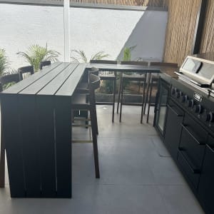 מטבח חוץ עם שולחן וכיסאות, גריל ותנור.