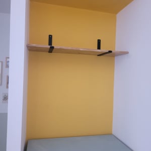 מדף עץ עם תומכים שחורים על קיר צהוב