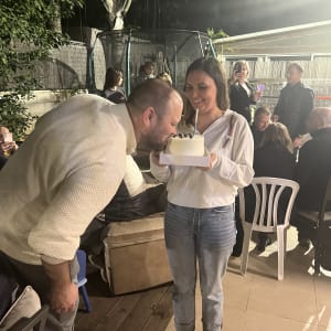 אישה מחזיקה עוגה עם נר, גבר מריח אותה