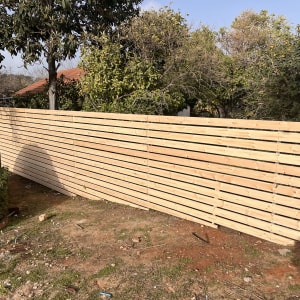 גדר עץ בגינה עם עצים ושיחים ברקע