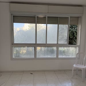 חלון גדול עם תריסים וכיסא פלסטיק לבן בחדר ריק