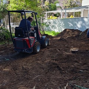 אדם נוהג בטרקטור קטן בחצר עם עצים מסביב