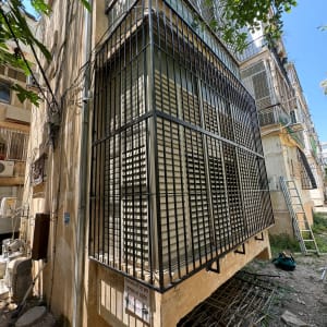 סורגים מתכתיים סביב חלון בניין עם תריסים