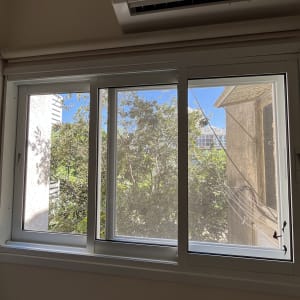 חלון נקי עם נוף לעצים ומזגן מעליו