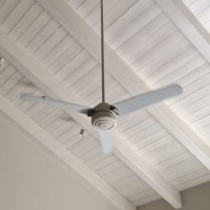 מאוורר תקרה מותקן על תקרה לבנה עם קורות עץ.