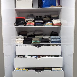 ארון בגדים מאורגן עם מדפים ומגירות מלאים בבגדים מקופלים.