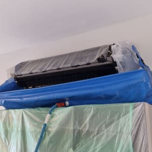 מזגן מכוסה בניילון כחול וירוק עם צינור מחובר