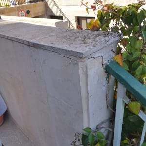 קיר עם סדקים וצמחייה ליד מעקה