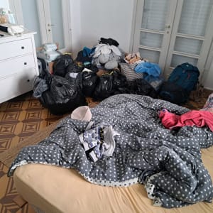 חדר עם שקיות זבל, בגדים מפוזרים ומגבות על מיטה