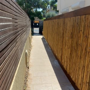 גדר עץ בצד שמאל, גדר במבוק בצד ימין, שביל מרוצף ביניהם