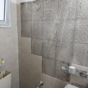 קיר אמבטיה עם אריחים מוסרים, כלי עבודה על מדף