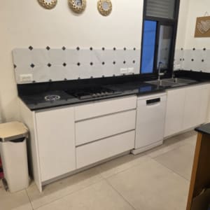 מטבח מודרני עם ארונות לבנים, משטח כהה וחיפוי קיר מקרמיקה