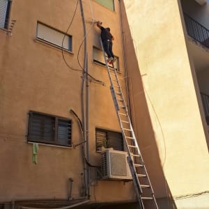 אינסטלטור עובד על סולם בתיקון או החלפת צנרת חיצונית בבניין מגורים