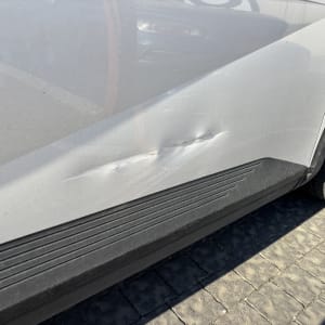 נזק לדלת רכב לבנה עם שריטות ושקעים.