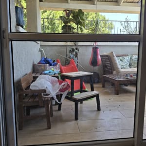 מרפסת עם רהיטי עץ וצמחייה מאחורי זכוכית