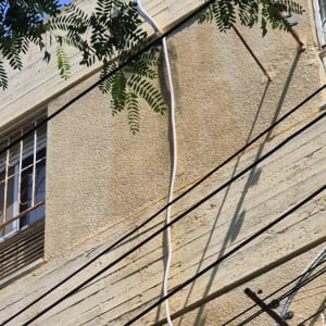 צינור מיזוג אוויר תלוי על קיר בניין עם צללים של עלים