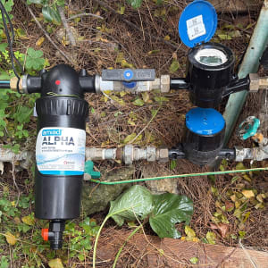 מסנן מים וצנרת בגינה עם צמחייה מסביב