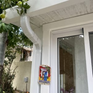 מרזב לבן מחובר לגג לבן עם עלים ירוקים