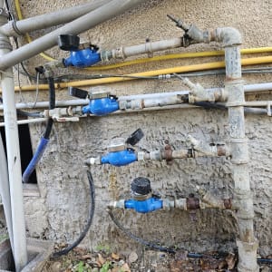 צנרת מים עם מדי מים כחולים מחוברים לקיר חיצוני